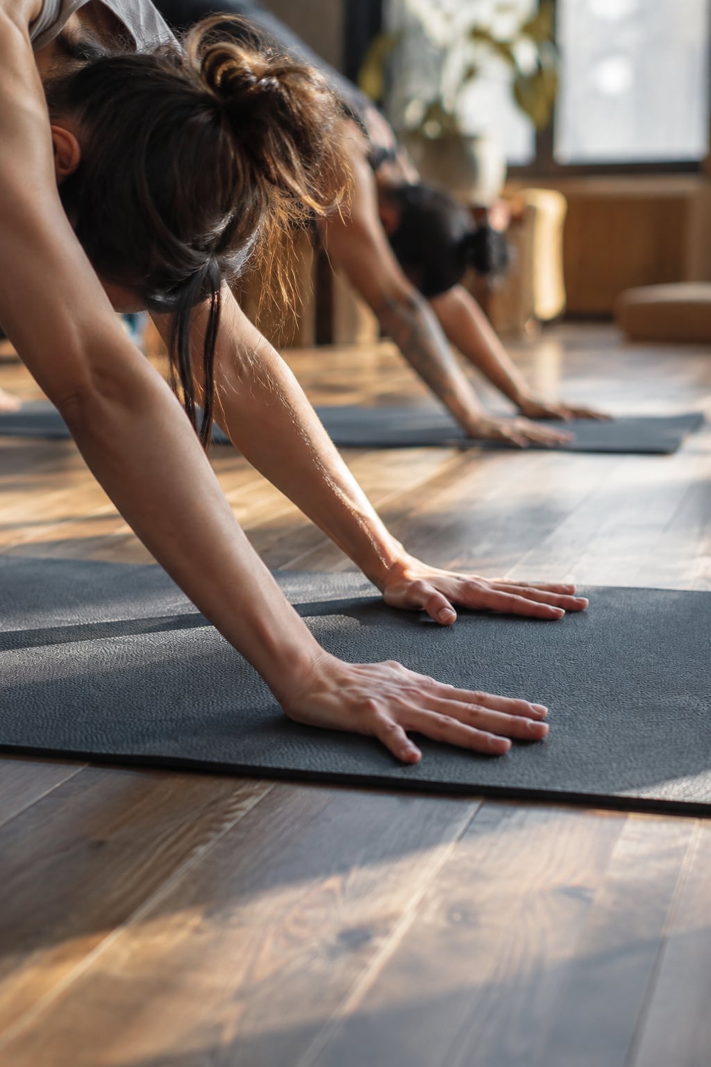 Hands spread and pressing into a yoga mat on a warm wood floor